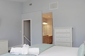 A bedroom with a bed, a dresser, a bathroom visible through an open door, and a light switch on the wall. - Barrier Dunes 542 - 55 - Relax N' Moore (Port St. Joe)
