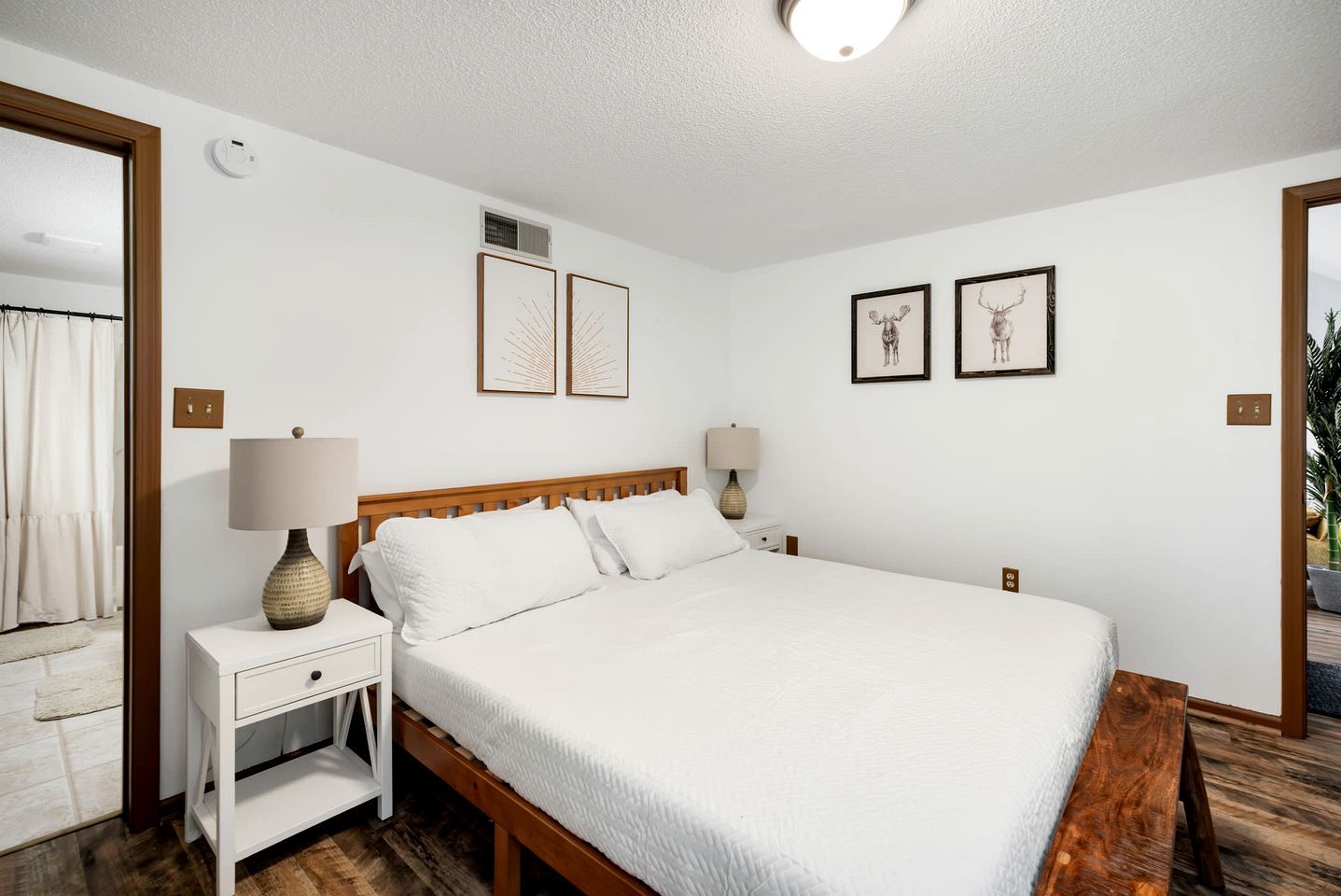 A bedroom with a wooden bed, white bedding, two bedside tables with lamps, and framed artwork on the walls.
