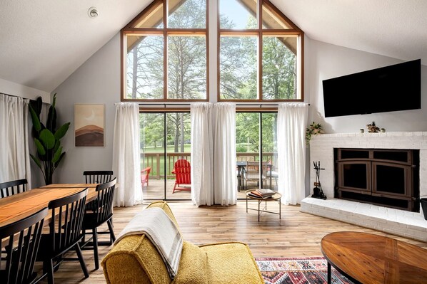 A spacious living room with a large window, a fireplace, and a dining area.
