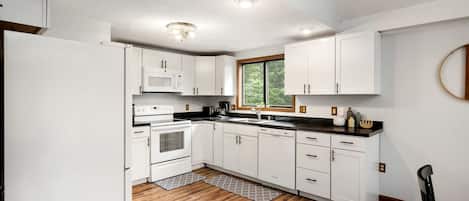 A modern kitchen with white cabinetry, a black countertop, and a wooden floor.