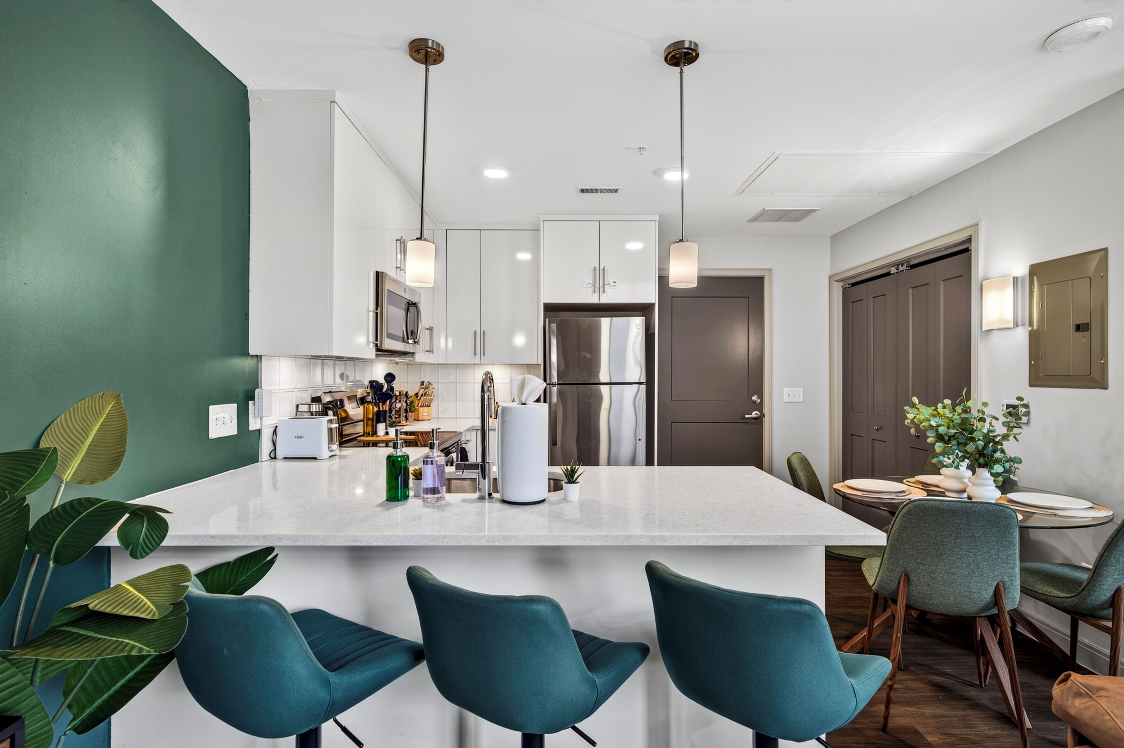 A modern kitchen with white cabinets, a central island, and teal chairs.