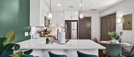 A modern kitchen with white cabinets, a central island, and teal chairs.