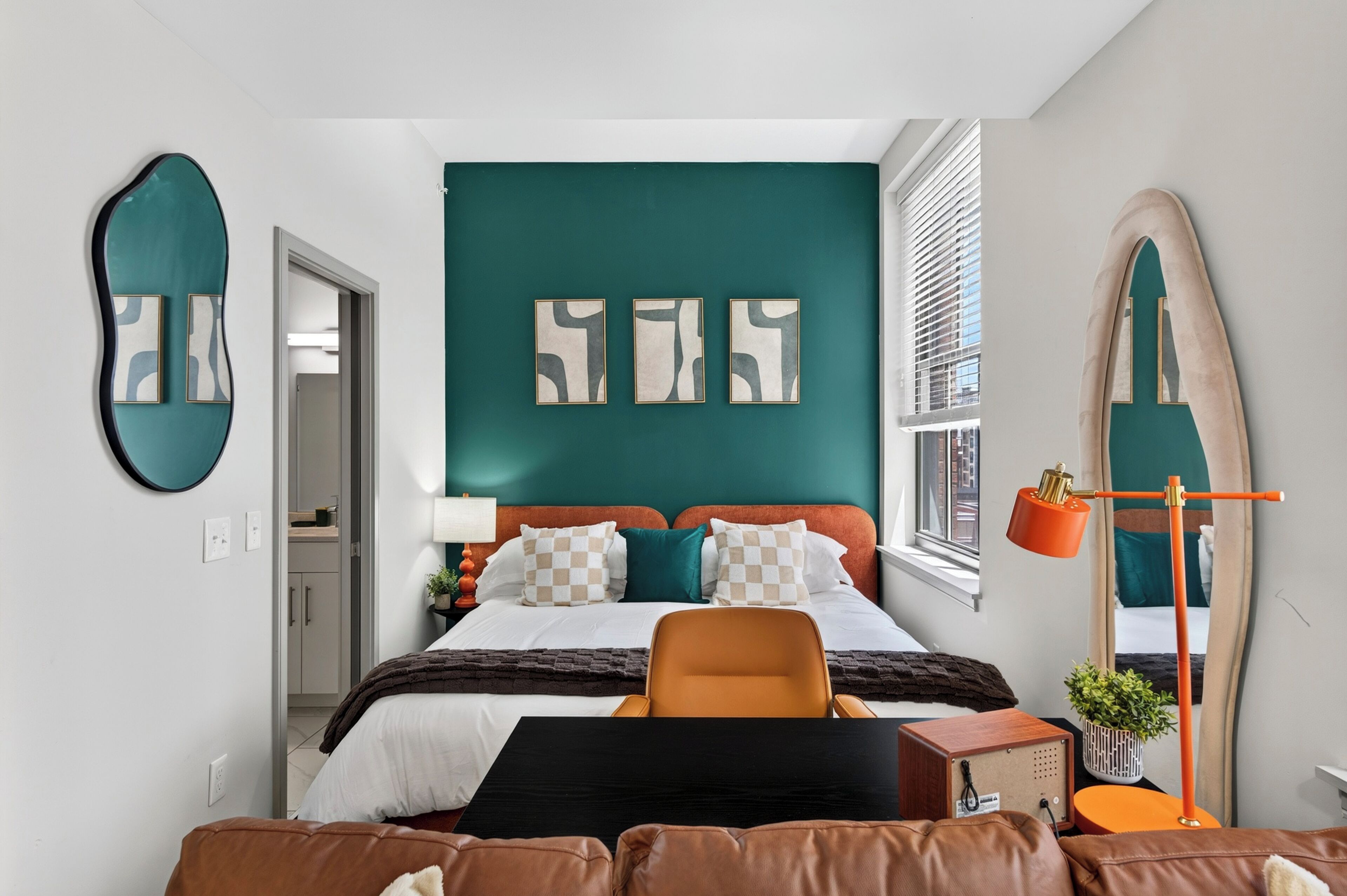 A modern bedroom with a bed, a chair, a desk, and a large mirror.