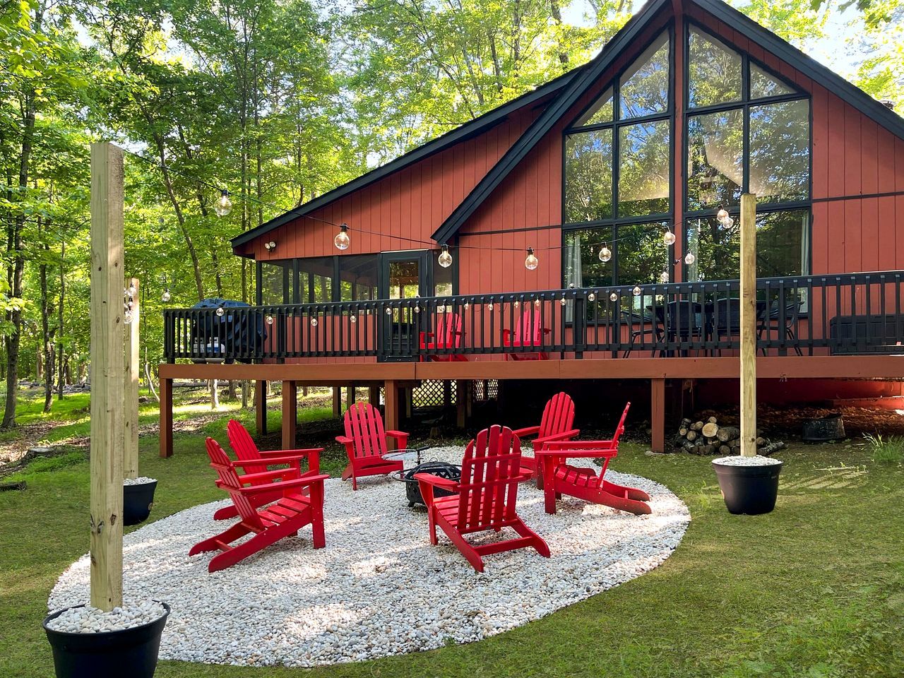 Een houten terras met rode Adirondack-stoelen en een vuurkuil, omringd door een grindpad.