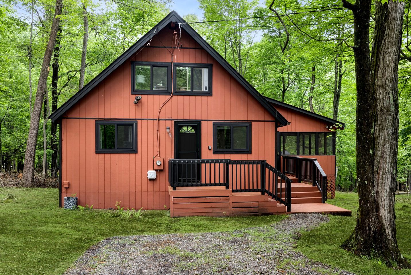 A two-story cabin with a front porch, surrounded by trees.