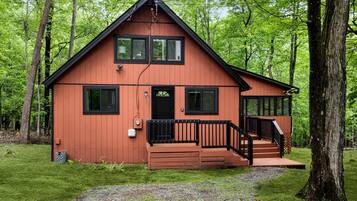 A two-story cabin with a front porch, surrounded by trees.