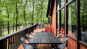 Terraza con una mesa y sillas, rodeada de grandes ventanales, con vistas a un área boscosa.