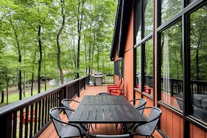 Une terrasse dotée d’une table et de chaises, entourée de grandes fenêtres et offrant une vue sur une zone boisée.