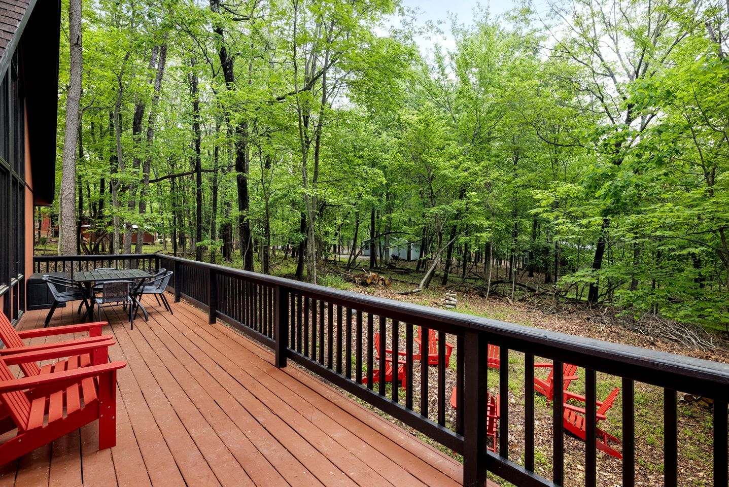 Um deck de madeira com mobiliário externo, rodeado por uma área arborizada.