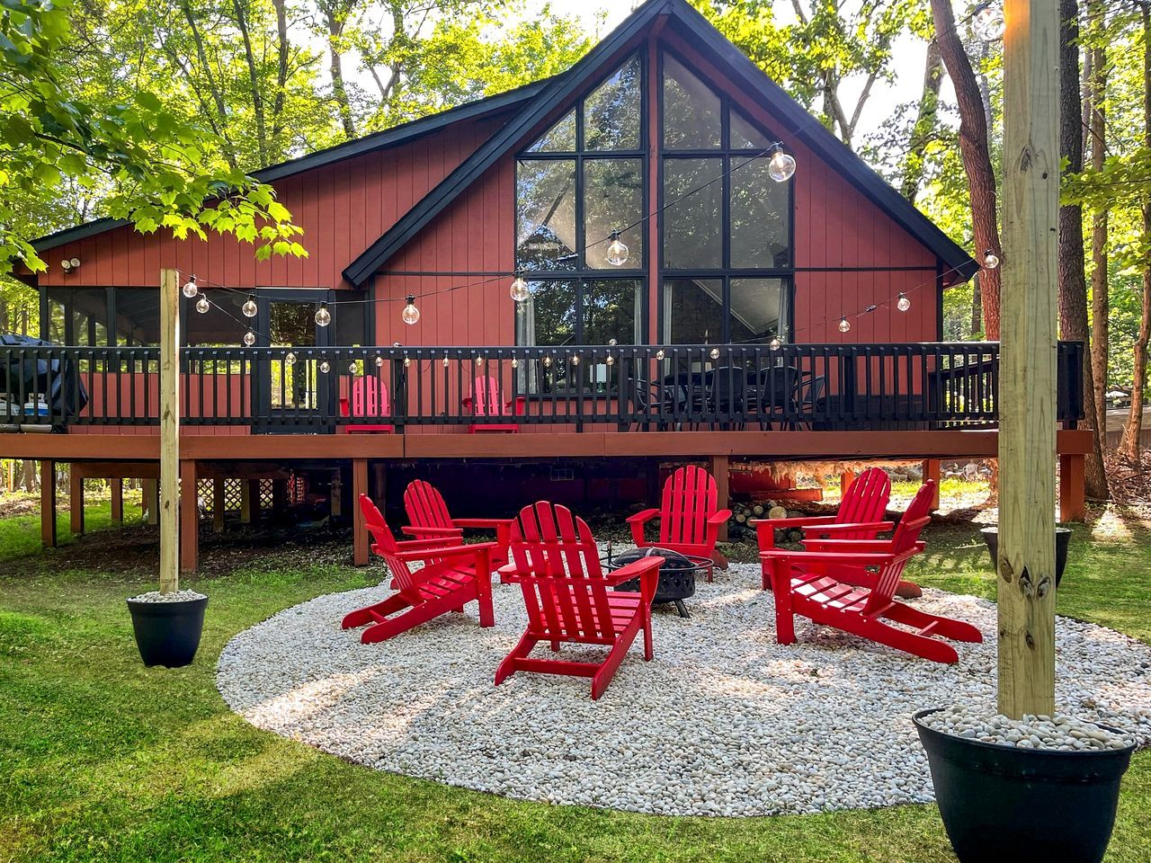 A red cabin with a balcony, surrounded by a gravel area with red Adirondack chairs.