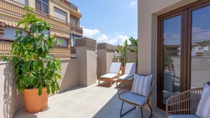 Ein Balkon mit zwei Korbstühlen, einem Blumentopf und einem gefliesten Boden.