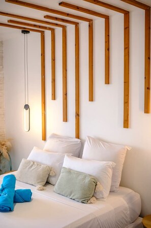 Un lit avec une literie blanche et plusieurs oreillers, un luminaire suspendu et des poutres en bois au mur.