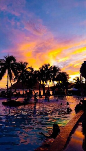 Un espace piscine agrémenté de palmiers et offrant une vue sur un ciel au coucher du soleil.