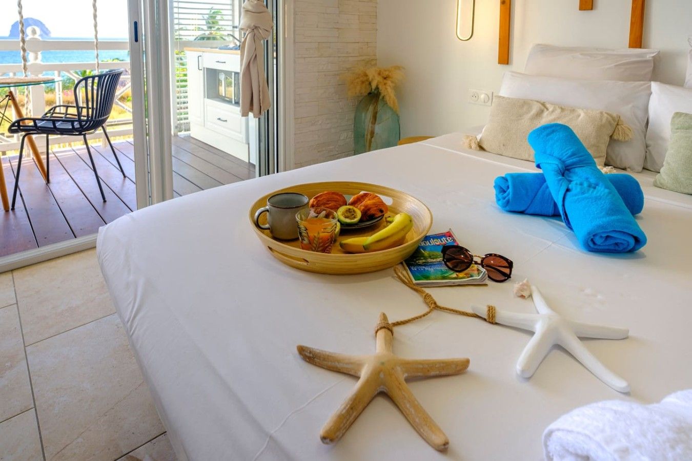 Habitación de hotel con cama, bandeja de desayuno, un par de gafas de sol y una decoración con forma de estrella de mar.