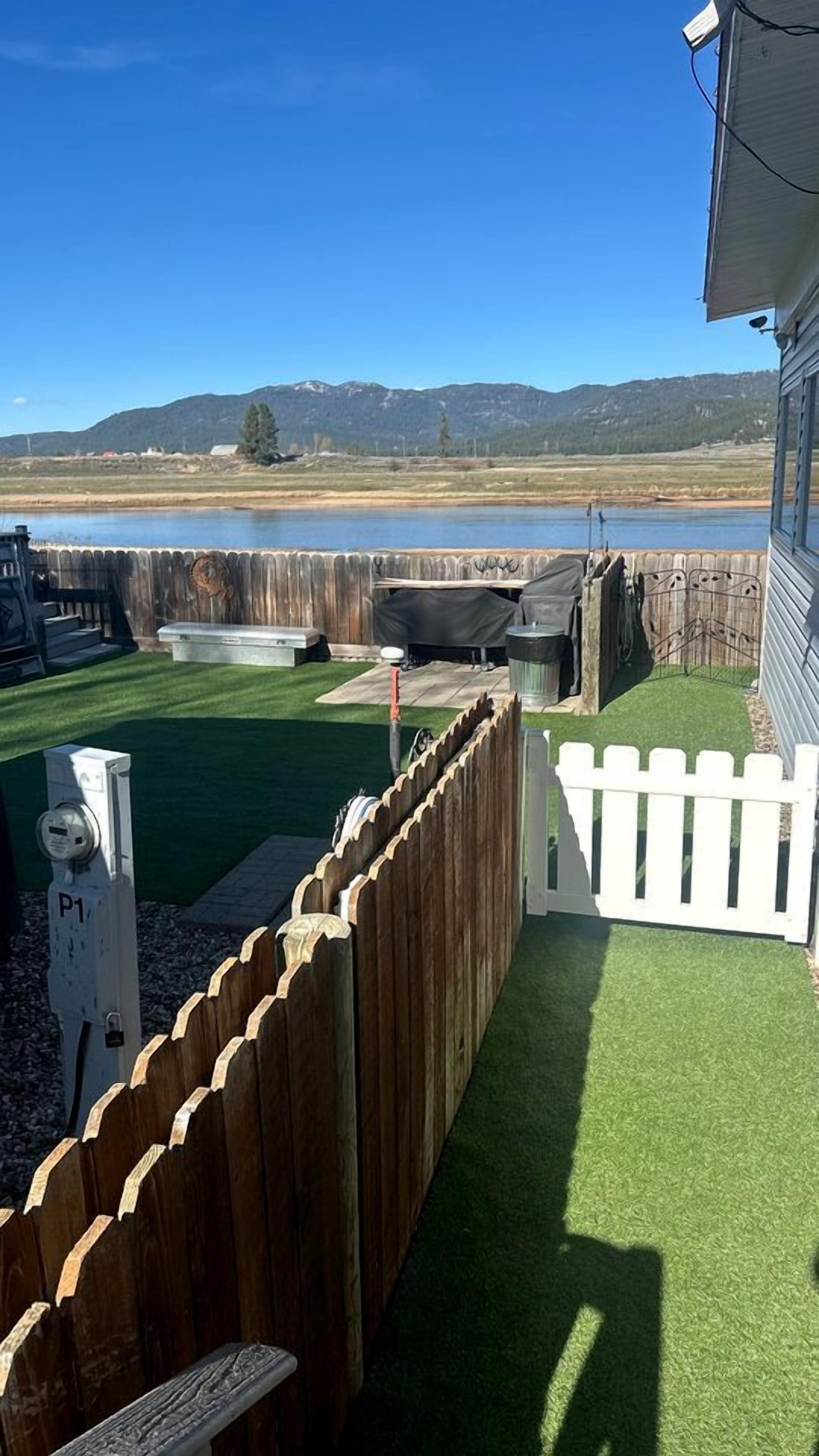 A backyard with artificial turf, a wooden fence, and a view of a lake and mountains.