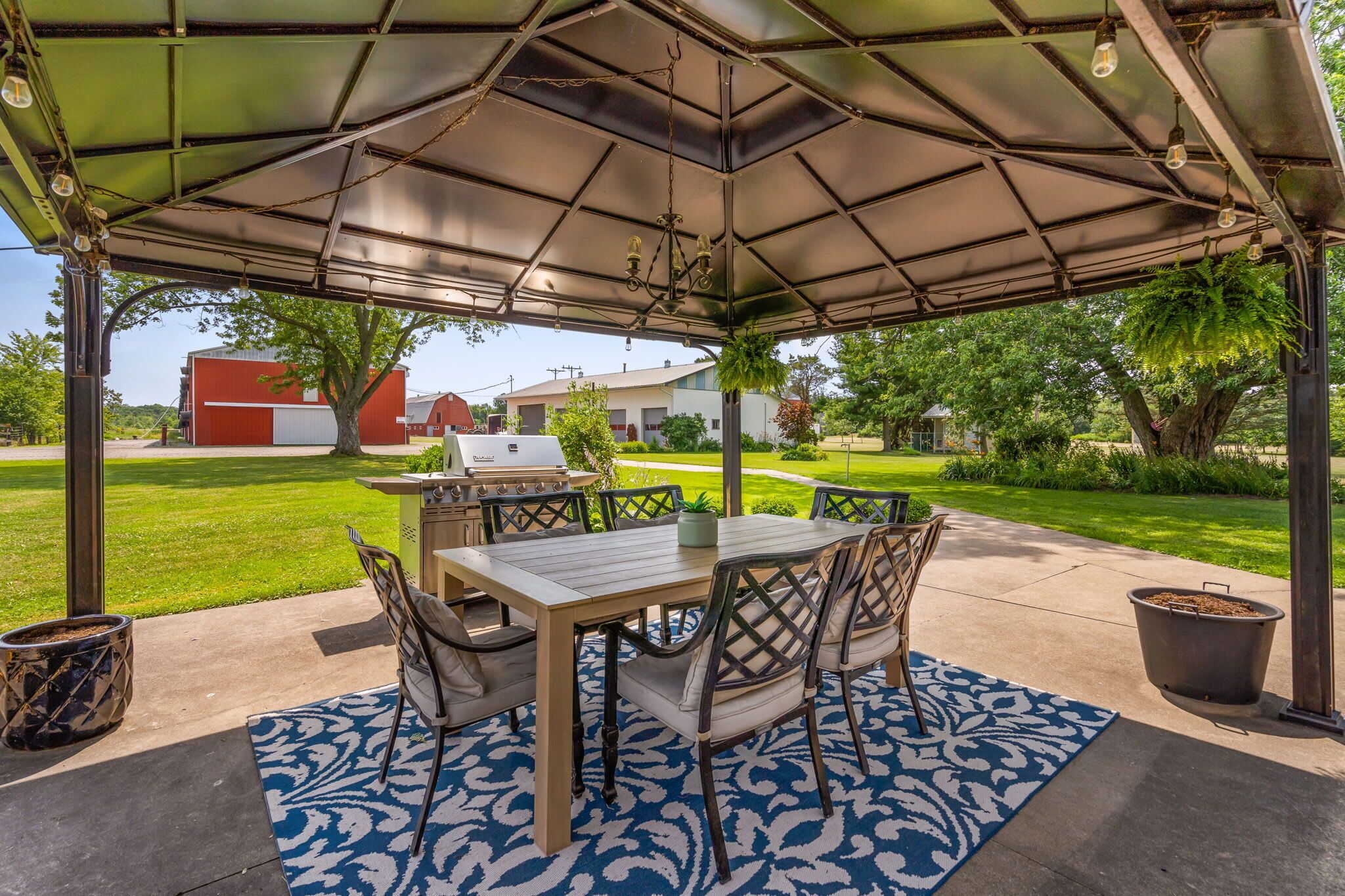An outdoor patio with a covered table and chairs, a grill, and a patterned rug.
