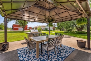 An outdoor patio with a covered table and chairs, a grill, and a patterned rug. - Spruce Valley Farm Retreat (Fort Erie)
