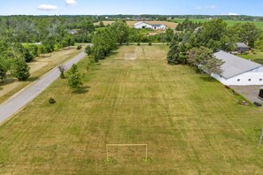 A large, open grassy field with a soccer goal in the center, surrounded by trees and buildings in the background. - Spruce Valley Farm Retreat (Fort Erie)