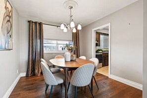 A dining room with a round table, four chairs, a chandelier, and a view of a kitchen through an open door. - Spruce Valley Farm Retreat (Fort Erie)