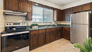 Una cocina con gabinetes de madera, un refrigerador de acero inoxidable, horno empotrado y una ventana con persianas.