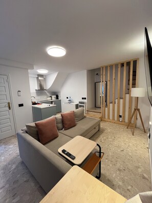 Ein modernes Wohnzimmer mit einem grauen Sofa, einem Holztisch und einem an der Wand befestigten Fernseher.