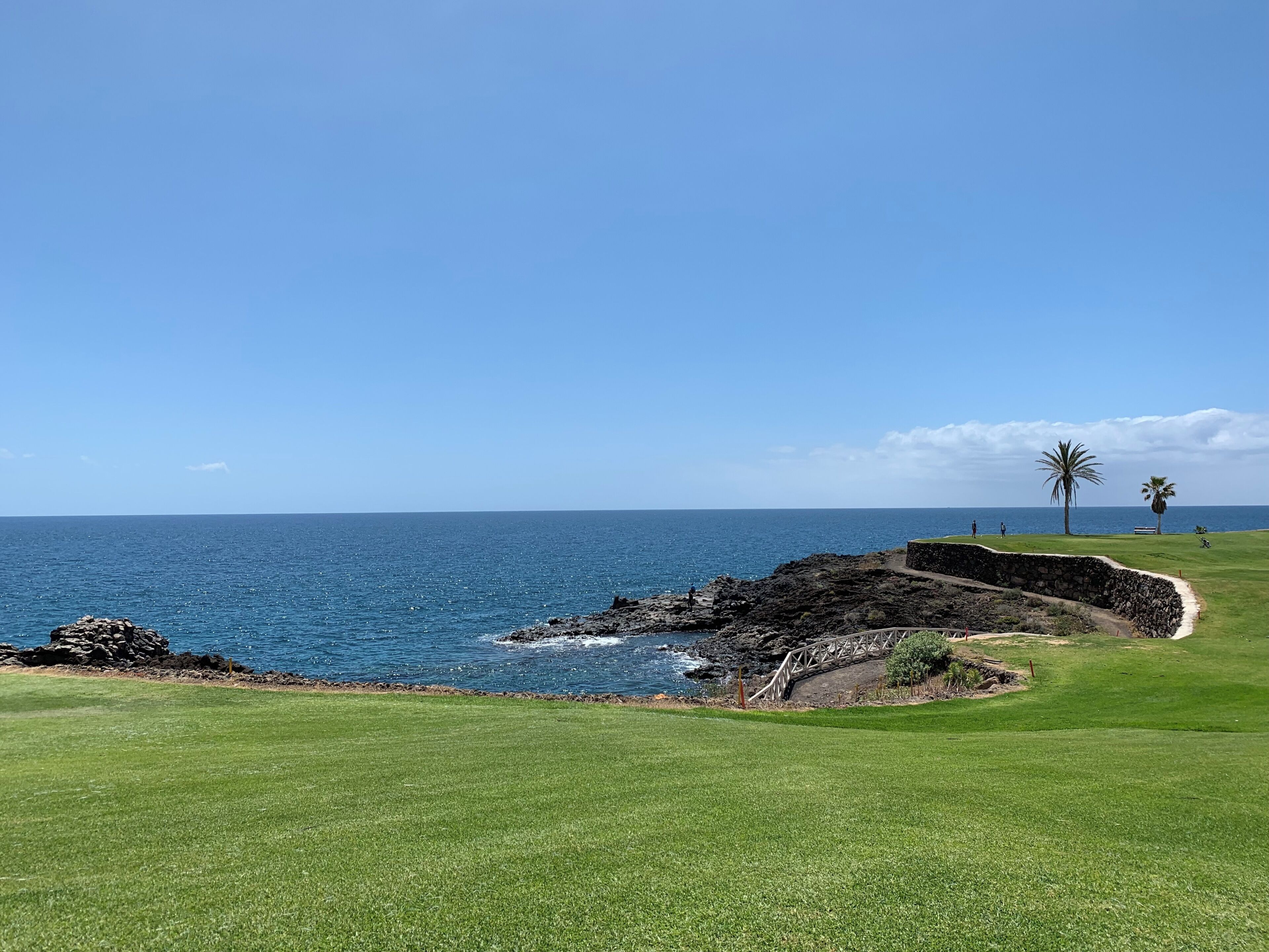 Ein Küsten-Golfplatz mit freiem Blick auf das Meer, eine Mauer aus Stein und ein gepflegter Grünfläche.