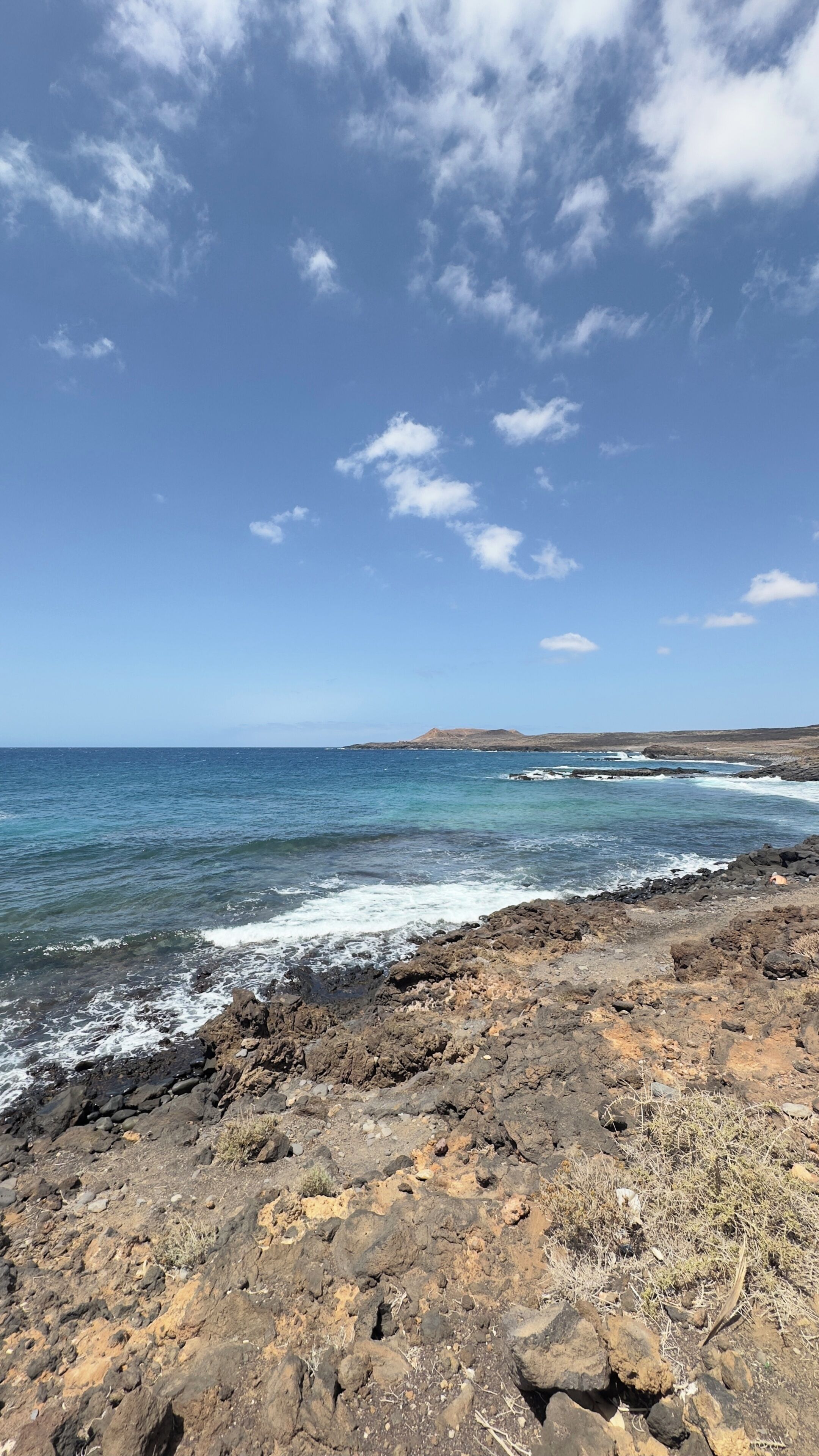 A rocky shoreline with waves crashing onto the rocks under a clear sky.