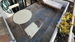 Un patio con mesa y sillas, una tumbona y un rincón con plantas en macetas.