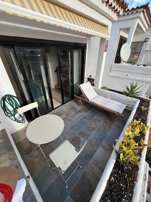 Eine Terrasse mit Tisch und Stühlen, einer Liege und einem Bereich mit Topfpflanzen.