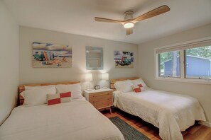 Une chambre avec deux lits, un ventilateur de plafond, une table de chevet avec une lampe et des œuvres d’art accrochées aux murs.