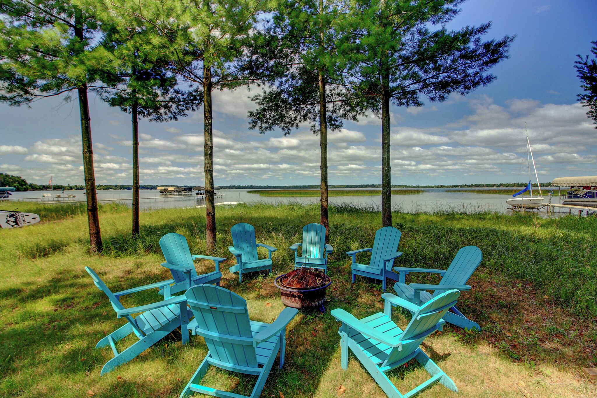A lakeside seating area with Adirondack chairs arranged around a fire pit.
