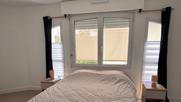 Una camera da letto con un letto, due comodini, una finestra con persiane e un lampadario.