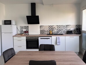 Eine moderne Küche mit Esstisch, schwarzen Stühlen, Backofen, Mikrowelle und Kaffeemaschine.