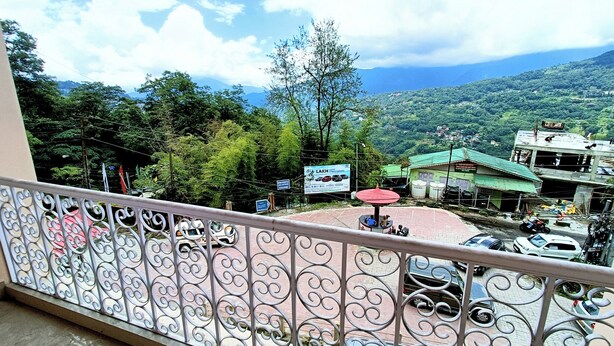 A balcony with ornate metal railings overlooking a mountainous landscape with buildings and parked cars.