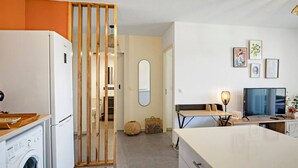 A modern kitchen with a washing machine, a dining area with a table and chairs, a TV, and a mirror on the wall. - Rosalia Apartment - Tropical Charm in Martinique (Fort-de-France)