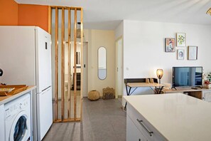 Eine moderne Küche mit Waschmaschine, ein Essbereich mit Tisch und Stühlen, einem Fernseher und einem Spiegel an der Wand.