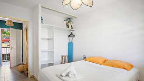 A bedroom with a bed, a wardrobe, a stool, and a hanging lamp. - Rosalia Apartment - Tropical Charm in Martinique (Fort-de-France)