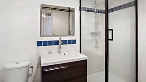 A bathroom with a white sink, dark wood vanity, a mirror, and a shower enclosure. - Rosalia Apartment - Tropical Charm in Martinique (Fort-de-France)