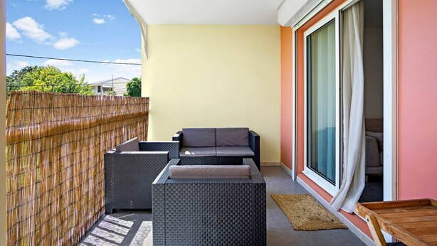 A balcony with a sofa, a small table, and a sliding glass door leading to a room. - Rosalia Apartment - Tropical Charm in Martinique (Fort-de-France)