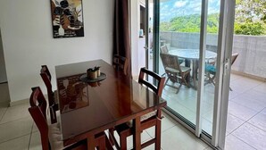 Una zona de menjador amb taula i cadires de fusta, llum penjant i una porta corredissa de vidre que dona a un pati exterior.