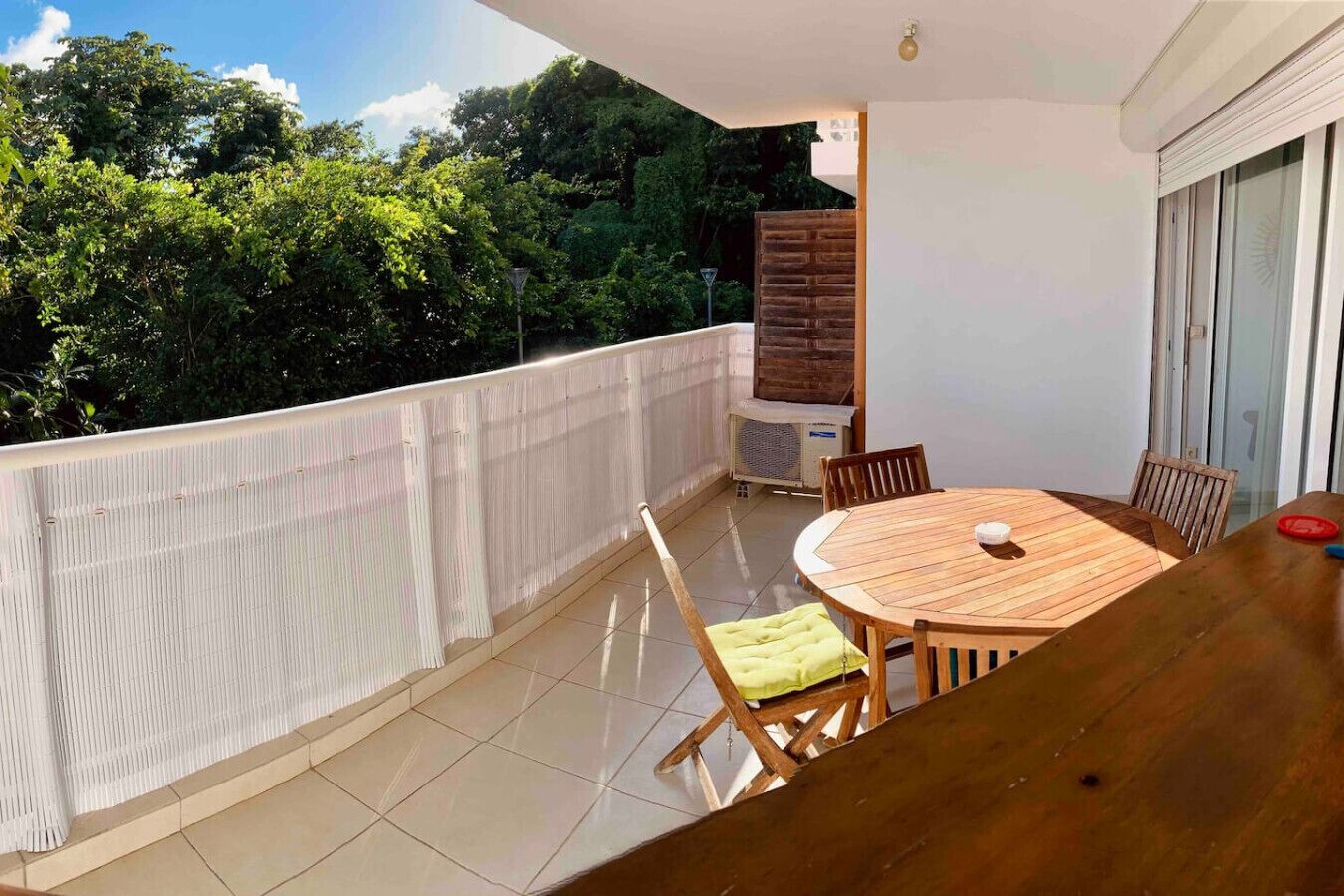 Ein Balkon mit einem runden Holztisch und Stühlen, einem weißen Geländer und Blick auf Bäume.
