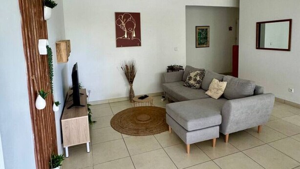 Un saló amb un sofà gris, una taula auxiliar petita, una televisió i una decoració mural.