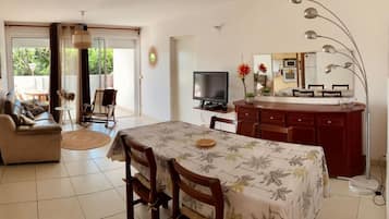 Ein Wohnzimmer mit einer Couch, einem Esstisch mit Stühlen, einem Fernseher und einer Küchenzeile mit einer Mikrowelle.