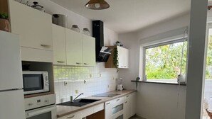 Una cuina amb armaris blancs, microones, forn, rentaplat i finestra amb vista a vegetació.