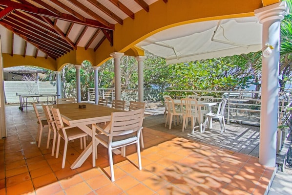 An outdoor patio with wooden tables and chairs, surrounded by white columns and covered by a white canopy.
