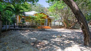 A yellow building with a porch, surrounded by trees and a sandy ground. - Yellow Beach Villa - Creole-style house on the beach (Le Diamant)