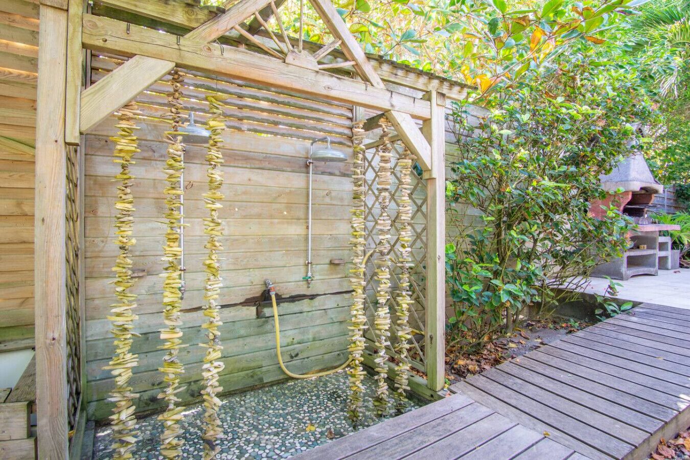 Una pérgola de madera con fuente de agua, rodeada de vegetación y una estructura de piedra.