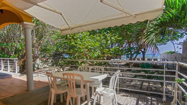 An outdoor seating area with a table and chairs under a canopy, overlooking a beach. - Yellow Beach Villa - Creole-style house on the beach (Le Diamant)
