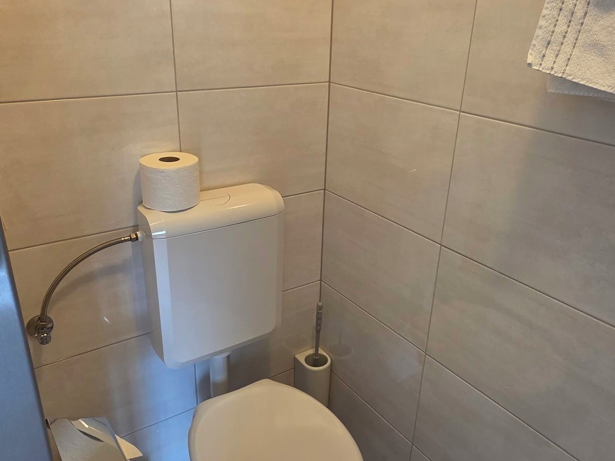 A bathroom with a toilet, a roll of toilet paper, and a hand dryer.