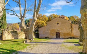 Edifici de pedra amb una entrada central, envoltat d'arbres i un camí de grava.
